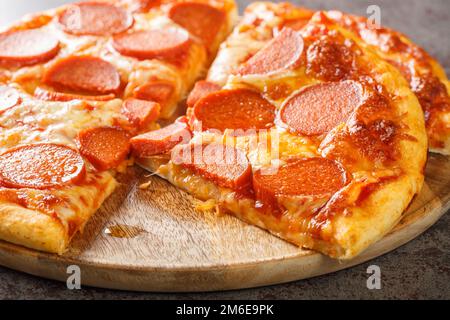 Délicieuse pizza au pepperoni tranché avec saucisse et fromage en gros plan sur une planche de bois sur la table. horizontale Banque D'Images