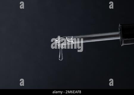 Pipeter avec du gel transparent liquide, du sérum ou de l'huile essentielle sur du noir Banque D'Images