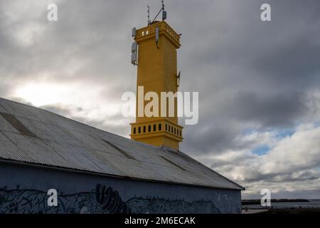 Toit d'un bâtiment et tour peinte en jaune d'un phare simple. Port de Sudurnesjabaer. Ciel nuageux et pluvieux intense. Sudurnesjabaer, Islande. Banque D'Images