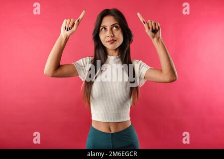 Jeune belle femme portant la récolte striée isolée sur fond rouge regarder vers le haut bouleversé, se sentir jaloux, regret, manquer bonne occasion, regarder Banque D'Images