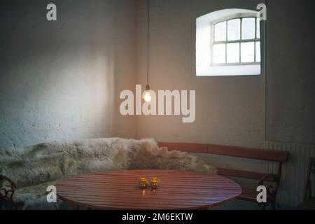 Ampoule simple suspendue sur une table en bois dans une ancienne écurie avec fenêtre Banque D'Images