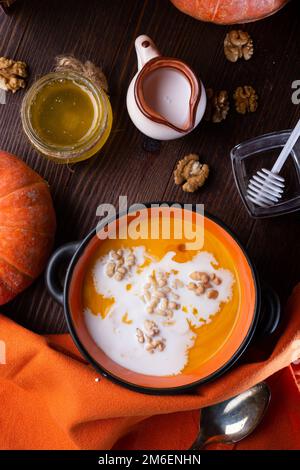 Coup d'État à la crème de citrouille cuite avec des noix, du lait de coco et du miel naturel servis dans un joli bol. servi sur une table marron en bois avec Banque D'Images