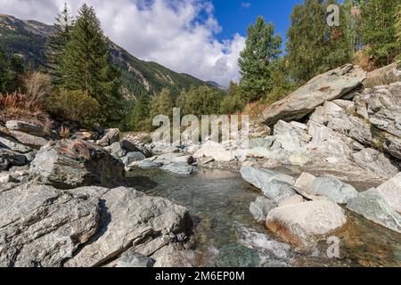 Ruisseau de glace de montagne parmi les roches de granit couvertes de forêt verte mixte, ciel bleu clair avec des nuages blancs de neige Banque D'Images