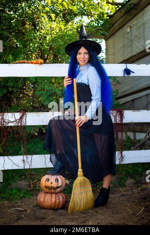 Jolie fille dans un costume de sorcière avec des citrouilles et un Un balai à une fête d'Halloween Banque D'Images