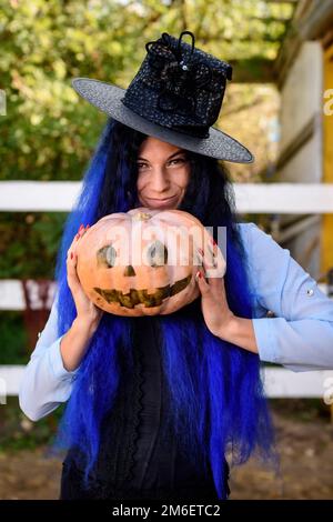 Une fille dans un costume de sorcière avec des cheveux bleus est tenant une citrouille avec un visage peint Banque D'Images