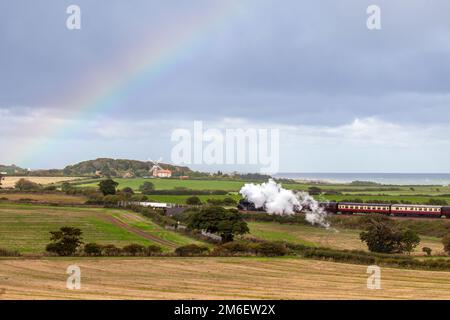 Train à vapeur Poppy Line dans le nord de Norfolk, en passant devant le moulin à vent de Weybourne avec un arc-en-ciel en arrière-plan en septembre 2022 Banque D'Images