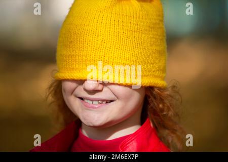 La petite fille a tiré un chapeau tricoté jaune sur ses yeux. La chute est arrivée. Banque D'Images