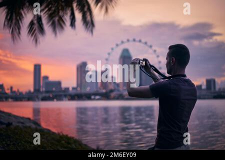 Homme photographiant les gratte-ciel urbains de Singapour au beau coucher du soleil. Tourisme avec appareil photo dans une ville moderne. Banque D'Images