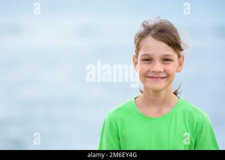 Portrait d'une fille heureuse de dix ans dans un t-shirt vert sur le fond de la mer Banque D'Images