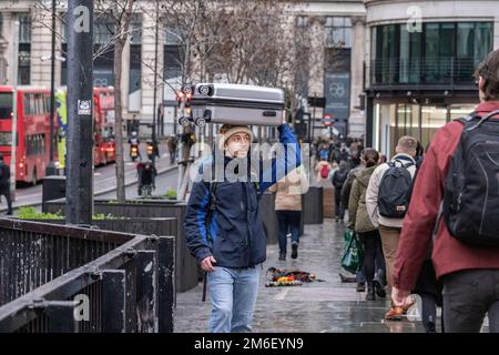 Un homme avec une valise sur sa tête traverse le London Bridge, City of London, Royaume-Uni Banque D'Images