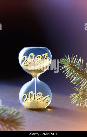 Fin de l'année 2023, Silverster, nouvel an 2024. HourGlass sur papier violet clair. HourGlass est également connu sous le nom de sablier, sablier ou sablier horloge. Banque D'Images