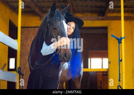 Une fille habillée comme une sorcière embrasse un cheval et regarde attentivement la distance Banque D'Images