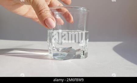Gros plan de la main femelle tenant le verre transparent à l'eau froide sur fond blanc Banque D'Images