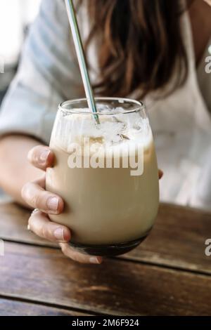 Latte à glace à la main. Un verre de café froid avec du lait dans la main d'une fille dans un café de ville d'été dans la rue. Boisson, style de vie, concept de ville. Photo de haute qualité Banque D'Images