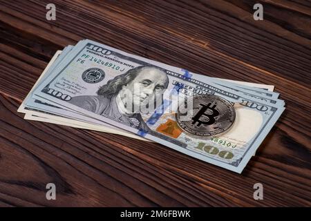 Pièce symbolique argent Bitcoin sur des billets de banque de cent dollars sur fond de bois. Échangez des bitcoins contre des dollars. Crypto-monnaie sur les États-Unis Banque D'Images