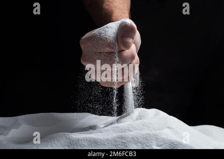 Homme avec une poignée de sable blanc sec dans ses mains, répande du sable à travers les doigts sur fond noir. Concept de flux de vie. Gros plan de grains de pur Banque D'Images