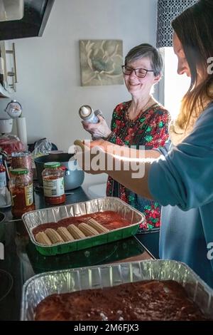 Deux femmes travaillent ensemble pour remplir les coquilles de pâtes de manucotti d'un mélange de fromage pour un plat de manucotti et de sauce marinara pour le dîner de la veille de Noël. Banque D'Images