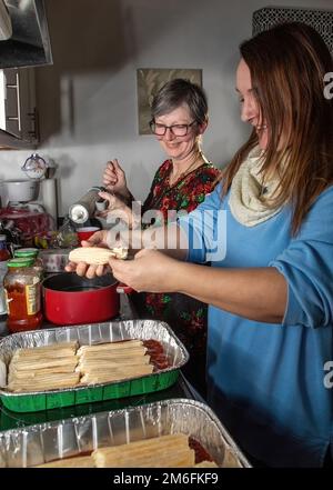 Deux femmes travaillent ensemble pour remplir les coquilles de pâtes de manucotti d'un mélange de fromage pour un plat de manucotti et de sauce marinara pour le dîner de la veille de Noël. Banque D'Images
