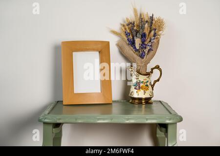 maquette de cadre photo vierge en bois avec verseuse rétro antique versante avec fleurs séchées sur un fond de table en bois vert uni Banque D'Images