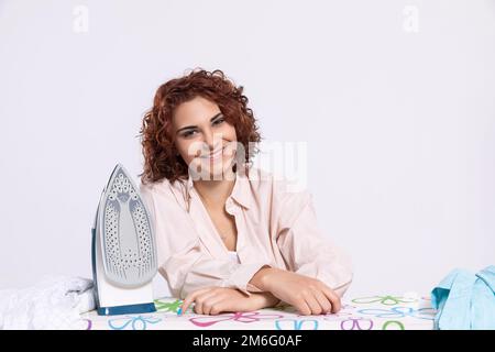 Une femme souriante s'assoit à la planche à repasser et au fer à repasser. Banque D'Images