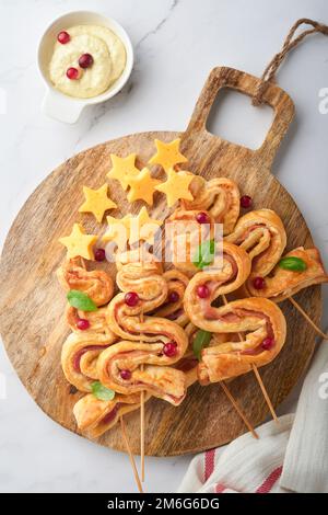 Hors-d'œuvre de Noël ou du nouvel an. Petits pains de pâte feuilletée en forme d'arbre de Noël avec fromage et jambon. Groupe de formes d'arbre de Noël sur panneau en bois. Carte d'identité festive Banque D'Images