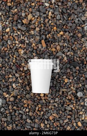 Une tasse de café ou de thé en papier blanc se trouve sur la côte rocheuse, cailloux Banque D'Images