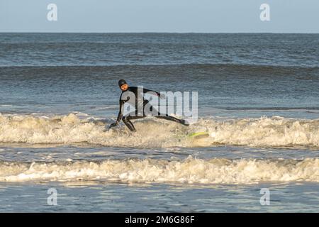 Surfeur mâle caucasien arrivant sur terre avec une combinaison noire, Cayton Bay, North Yorkshire, Royaume-Uni Banque D'Images