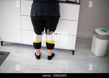 Les jambes des femmes avec des leggings et des chaussettes jaunes et blancs noirs se trouvent devant un placard. Photo de haute qualité Banque D'Images