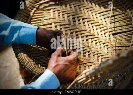 Un artisan qualifié travaillant manuellement un fauteuil en bambou détaillé avec ses doigts et ses outils Banque D'Images