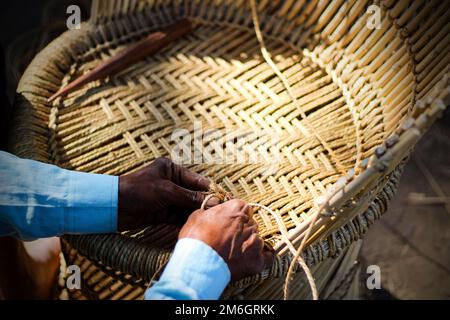 Un artisan qualifié travaillant manuellement un fauteuil en bambou détaillé avec ses doigts et ses outils Banque D'Images