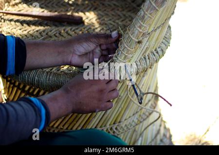 Un artisan qualifié travaillant manuellement un fauteuil en bambou détaillé avec ses doigts et ses outils Banque D'Images