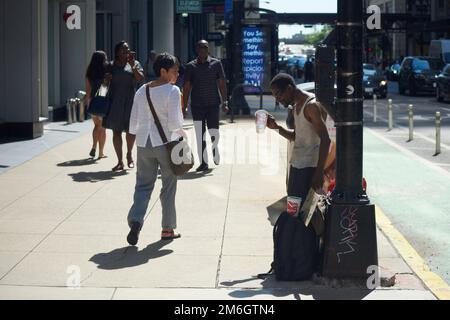 Un homme noir supplie le changement et les dons du public au soleil sur un coin de rue dans la zone du parc du Millénaire de Chicago en été Banque D'Images