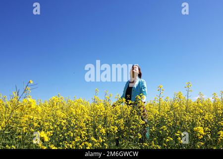 Une femme dans un champ avec des fleurs jaunes sur fond bleu ciel Banque D'Images