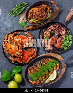 Ensemble de plats de fruits de mer. Crabes, poulpes, calmars et crevettes tigrées sur des casseroles en fonte et des assiettes sur fond noir. Vue de dessus Banque D'Images