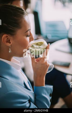 Gros plan d'une belle femme d'affaires qui boit du matcha latte tout en étant assise au café Banque D'Images