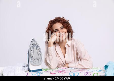 Une femme souriante s'assoit à la planche à repasser et au fer à repasser. Banque D'Images