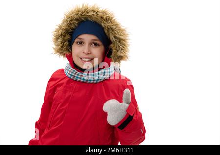 Adorable jeune garçon dans une parka rouge en duvet avec capuche en fourrure, en train de monter, en souriant, en regardant l'appareil photo, isolé sur fond blanc Banque D'Images