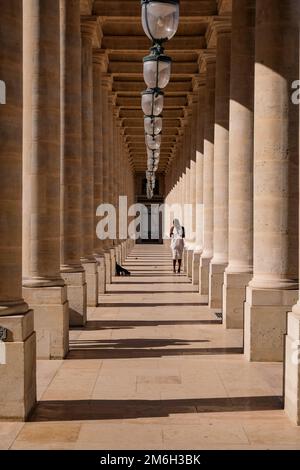 Jeune Noire posant pour des photos dans une robe blanche aux colonnes du Palais Royal à Paris, France - mode, influenceur Banque D'Images