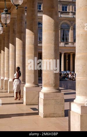 Jeune Noire posant pour des photos dans une robe blanche aux colonnes du Palais Royal à Paris, France - mode, influenceur Banque D'Images