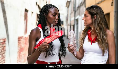 deux jeunes amis blancs et noirs parlent dans la rue avec une certaine intimité pendant les festivités d'une ville en espagne. concept d'amitié, Banque D'Images