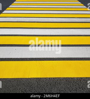 Passage piéton fraîchement peint avec des marquages jaunes et blancs sur l'asphalte, photo verticale, lumière du soleil Banque D'Images