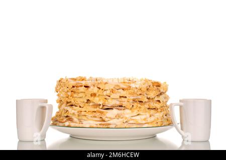 Un gâteau à la crème maison sur un plat en céramique avec deux tasses de café, macro, isolé sur fond blanc. Banque D'Images