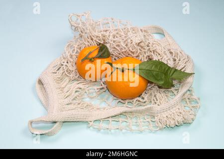 Mandarines mûres dans un sac à ficelle sur fond bleu. Fruits dans un emballage écologique Banque D'Images