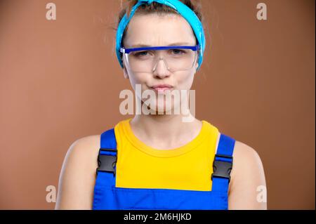 Une belle jeune femme caucasienne avec des cheveux blonds dans des lunettes et des vêtements spéciaux semble avec scepticisme à l'égard de la caméra Banque D'Images