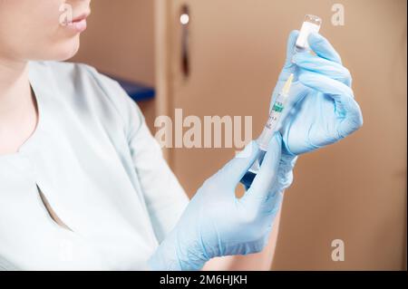 Une jeune femme de race blanche vêtue de vêtements médicaux et de gants en caoutchouc sans masque protecteur est en train de tirer un vaccin ou un médicament f Banque D'Images