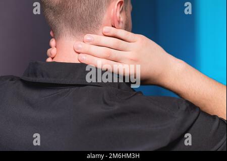 Gros plan. Un homme freelance dans une chemise sombre a un mal de cou après avoir travaillé longtemps, il se moque de son cou lui-même. Banque D'Images