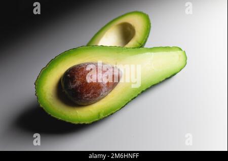 Légumes frais - Zutano avocat sur une table blanche avec un fond noir. Image contrastée d'un légume savoureux Banque D'Images