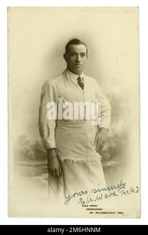 Original post WW1 ans studio portrait carte postale d'une épicerie ou laiterie assistant / propriétaire, portant un tablier, et une chemise et une cravate. Du studio d'Alice (Maud) Gibson au 299 Holderness Road, Hull, Yorkshire, Angleterre, Royaume-Uni. Vers 1919. Banque D'Images