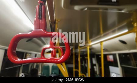 Main courante suspendue rouge au plafond pour les passagers debout pendant le transport. Transports publics urbains et suburbains modernes. Bus vide. Banque D'Images