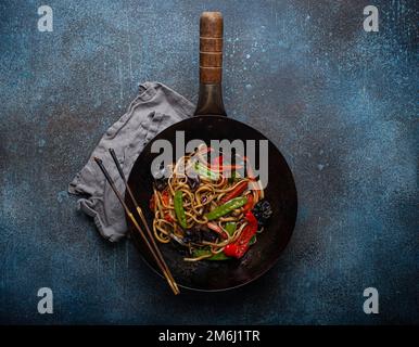 Faites sauter les nouilles asiatiques avec les légumes dans un wok noir Banque D'Images